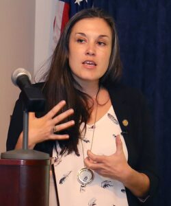 Image of Dr. Rebekka King speaking behind a microphone, gesturing with her hands.