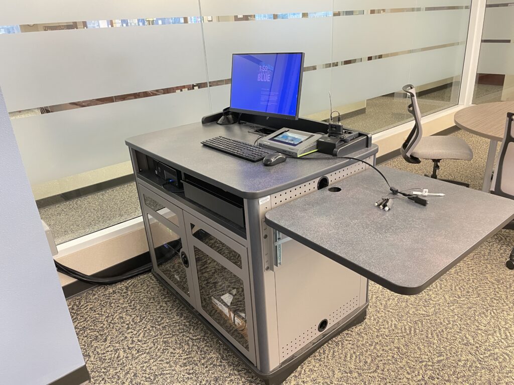 The Center for Teaching and Mentoring's workstation with a Dell desktop computer, connected display monitor, and a laptop docking station positioned on a podium‑style desk.