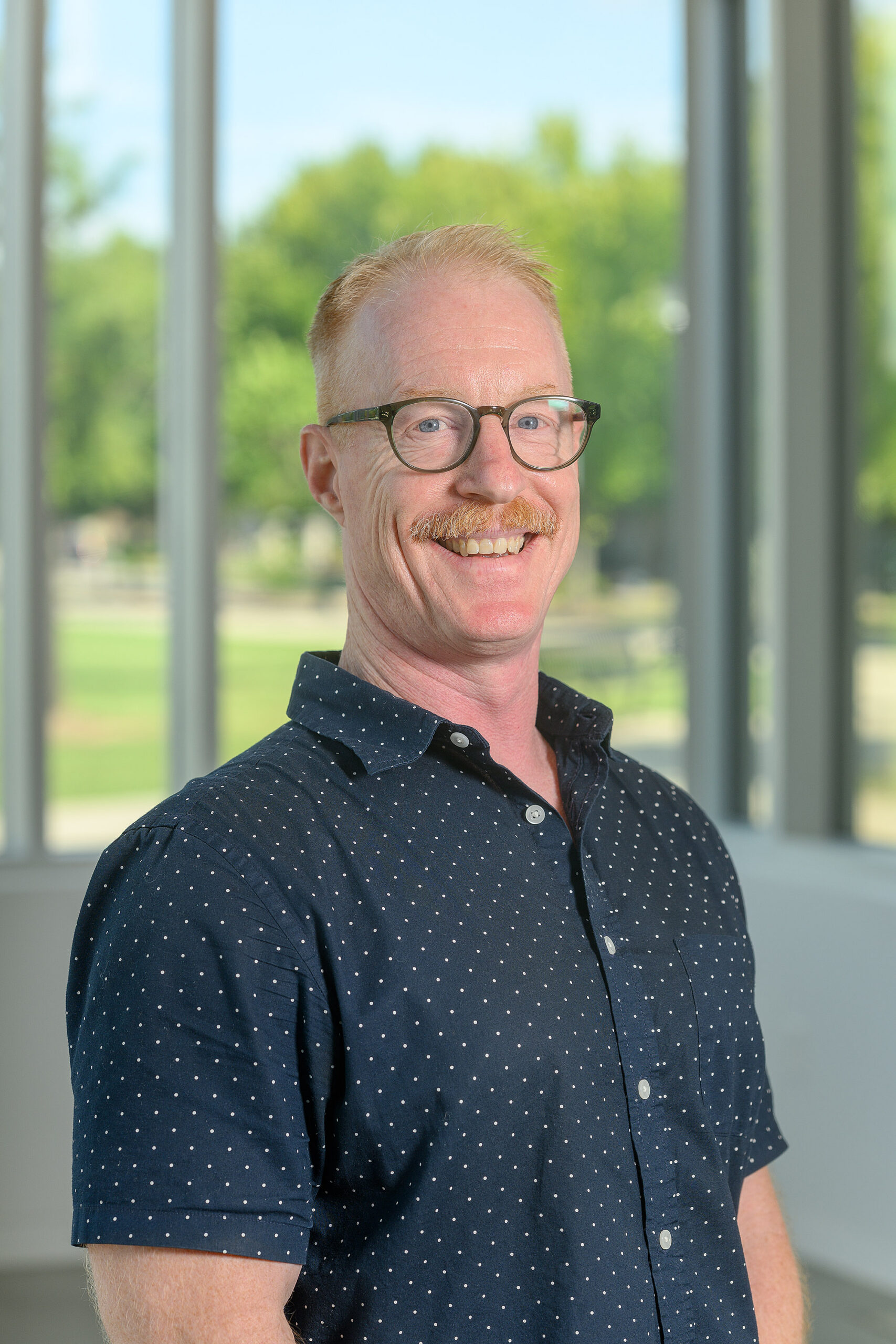 Photograph of Rudy Dunlap, Provost Fellow at MTSU, standing indoors with green grass and trees seen through a window behind him